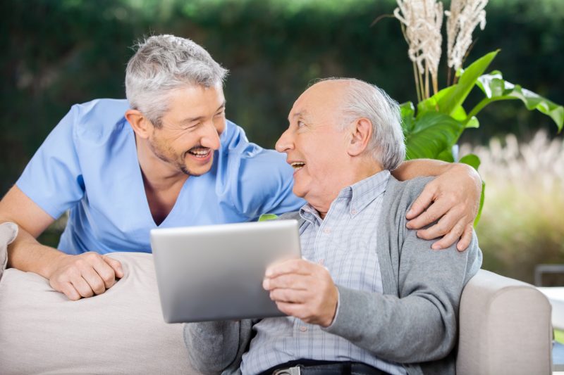 Laughing,Male,Caretaker,And,Senior,Man,Using,Tablet,Computer,At